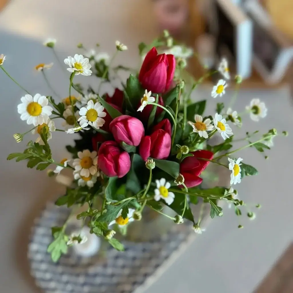 Person arranging fresh-cut flowers on a white table with greenery and blooms laid out