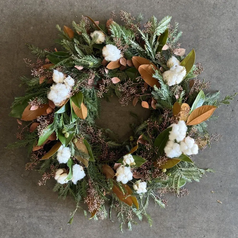 Completed DIY holiday wreath from Kit #2 featuring cotton branches, magnolia leaves, and warm rustic botanicals on grapevine base hanging display