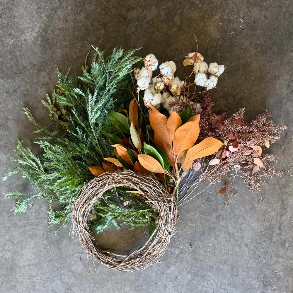 Holiday Wreath Kit #2 unassembled materials including grapevine wreath base, redwood foliage with cones, magnolia tips, dried cotton branches, and gold seeded eucalyptus laid out on gray surface