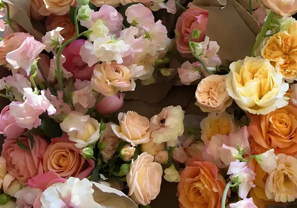 Assorted fall wedding flowers with peach, yellow, and pink roses mixed with ranunculus and lisianthus