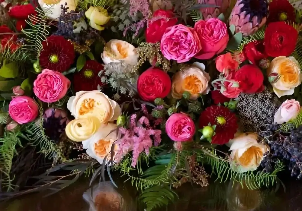 Bulk garden roses in pink, peach, and red tones arranged in a lush wedding centerpiece with mixed florals and greenery