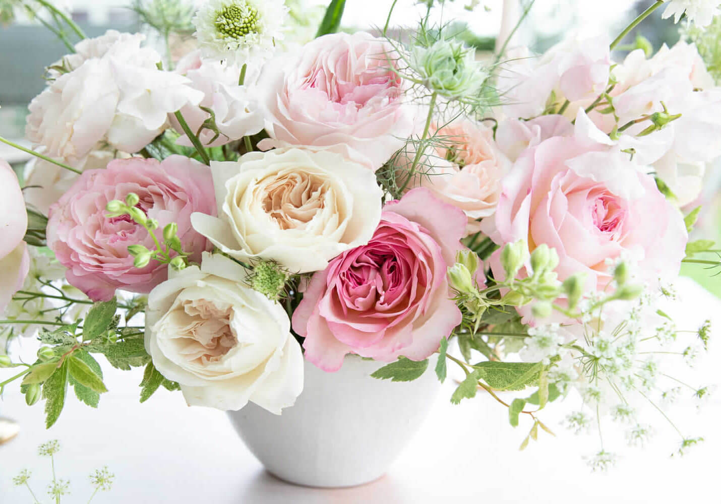 Pink and white bulk garden wedding roses arranged in a white vase with greenery
