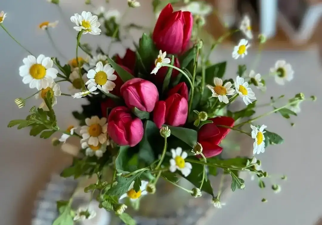 Person arranging fresh-cut flowers on a white table with greenery and blooms laid out